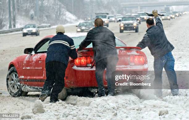 An unidenitifed man signals for traffic to slow down as he and two other men push a car back onto the highway after it slid onto the median during a...