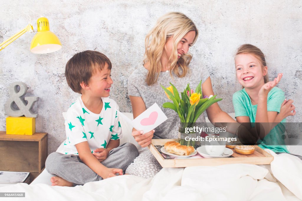 Mother´s Day - two children surprise their mother with breakfast in modern bed