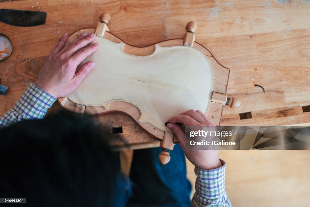 Close up of a craftsman carving the body of a violin from wood