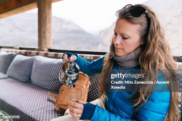 woman pouring tea in glass on balcony of mountain hut - imlil morocco photos et images de collection
