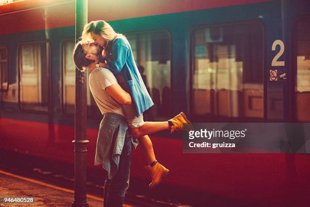 passionate young man and woman kissing beside the train at the railway station - romance stock pictures, royalty-free photos & images
