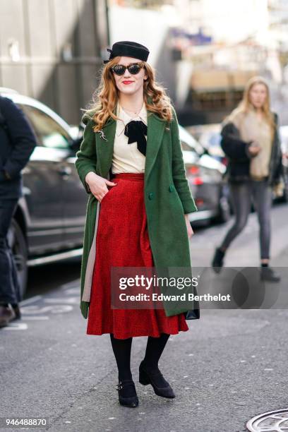 Guest wears a black hat, a green coat, a shirt, a red skirt, black shoes, during London Fashion Week February 2018 on February 16, 2018 in London,...