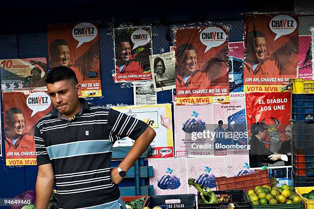 Man stands at a produce stand in front of Hugo Chavez campaign posters in Caracas, Venezuela on Saturday December 2 one day before presidential...