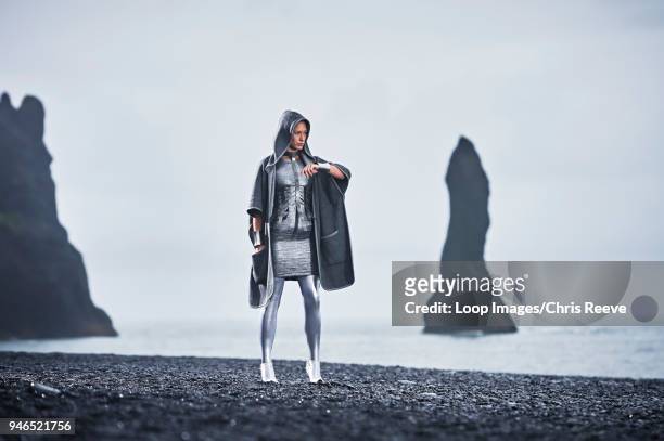 cloaked young women in silver outfit standing with confidence in front of basalt rock in southern iceland - silver dress photos et images de collection