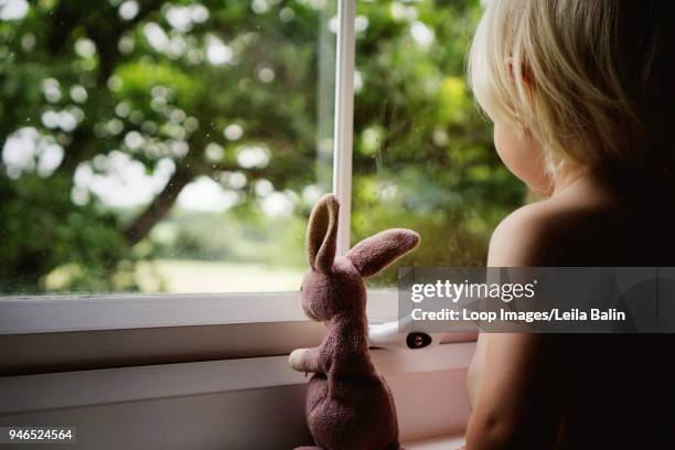 boy looking out of bedroom window with his stuffed bunny rabbit - balin stock pictures, royalty-free photos & images