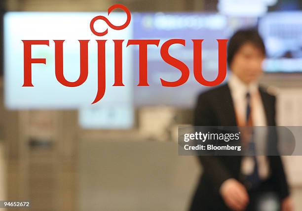 An employee walks behind the logo for Fujitsu Ltd. At the company's offices in Tokyo, Japan, on Tuesday, Dec. 4, 2007. Fujitsu Ltd., Japan's biggest...