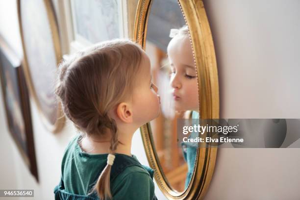 child puckering up at her own reflection in a mirror, whilst steaming the glass with her breath - zichtbare adem stockfoto's en -beelden