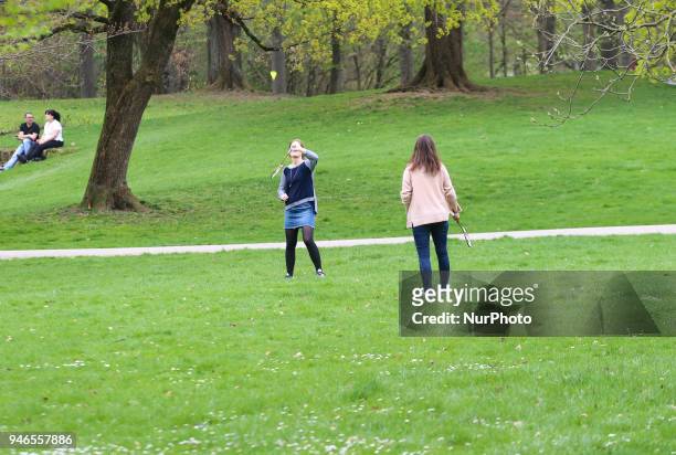 Two young woman play badminton on a weed on a cloudy spring day in Munich.