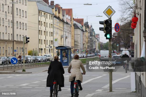 Two women ride their bikes next to a green traffic light on a cloudy spring day in Munich.