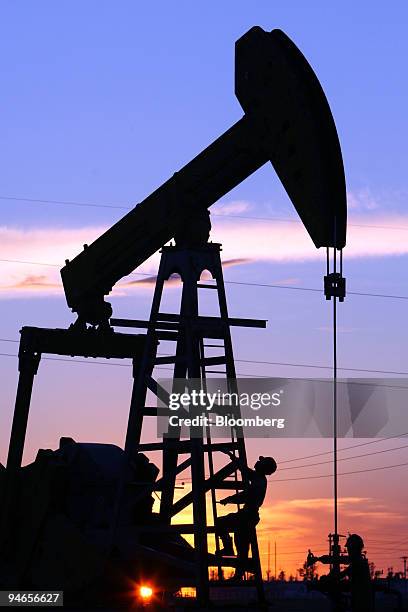Maintenance workers work on a CNPC "nodding donkey" oil pump at sunset in an oilfield outside Daqing, Heilongjiang province, China, on July 13, 2006....