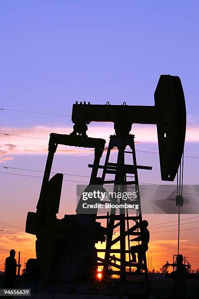 Maintenance workers work on a CNPC "nodding donkey" oil pump at sunset in an oilfield outside Daqing, Heilongjiang province, China, on July 13, 2006....