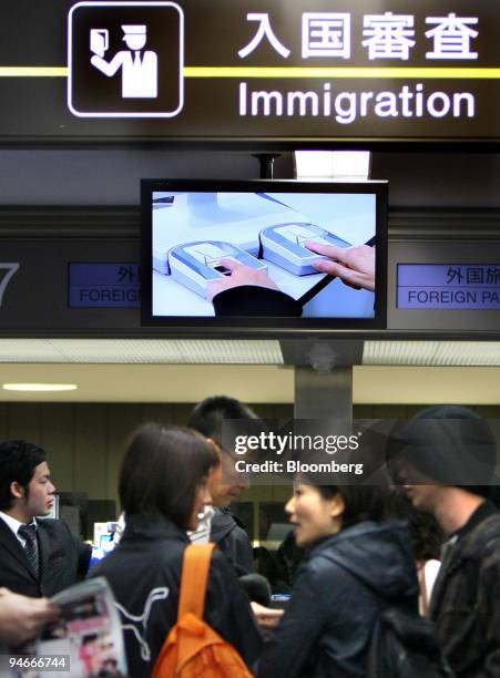 Travellers gather under a screen showing fingerprints being read at the immigration area of Narita International Airport in Chiba prefecture, Japan,...