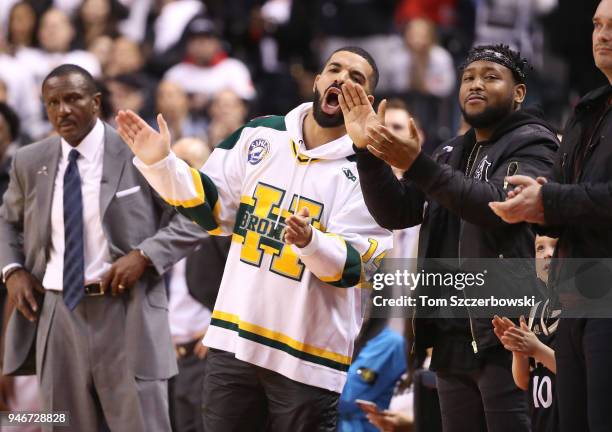 Rap artist Drake reacts as head coach Dwane Casey of the Toronto Raptors looks on during their victory against the Washington Wizards during Game One...