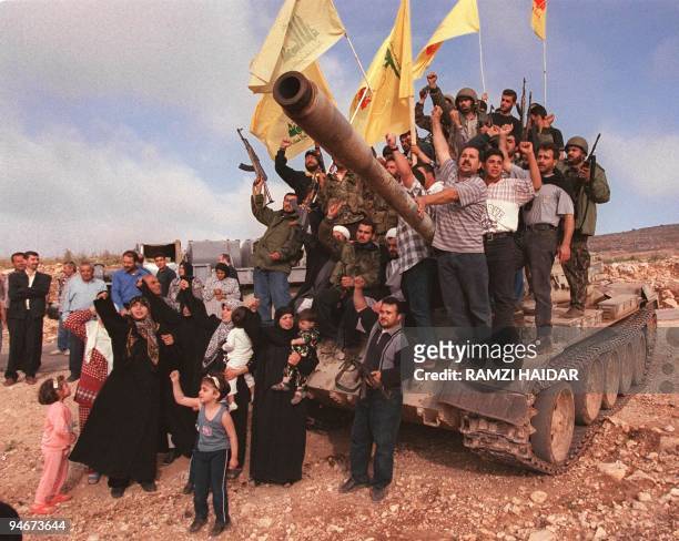 Lebanese villagers and Hezbollah fighters pose for a picture on and around a tank, abandoned by the Israeli-allied South Lebanon Army militia 24 May...