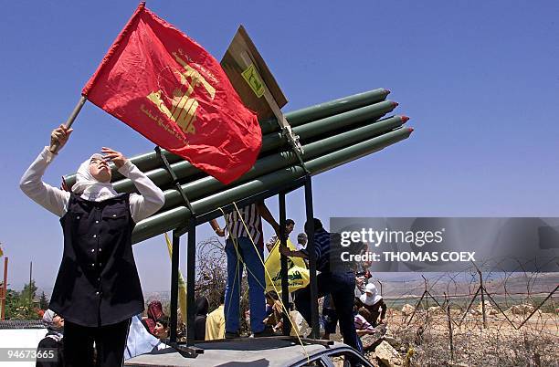 Lebanese woman waves the flag of Hezbollah in front of a fake missile-launcher 25 May 2000 behind the barbed wire at the border between Lebanon and...