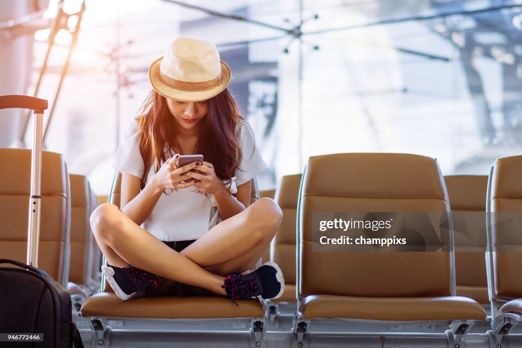 Adolescente de mulher asiática usando smartphone no aeroporto terminal sentado com mala de bagagem e mochila para viajar no verão férias relaxantes esperando transporte de voo