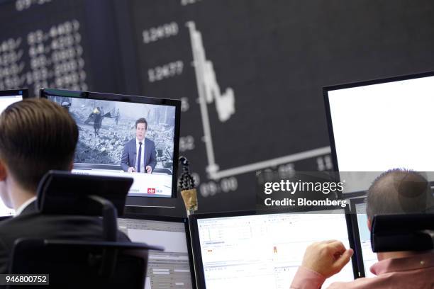 Television news report shows damage from military airstrikes on Syria as the DAX Index curve is displayed beyond at the Frankfurt Stock Exchange,...