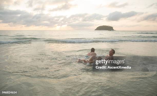 men laugh after tackling each other into sea - shorts down stock pictures, royalty-free photos & images