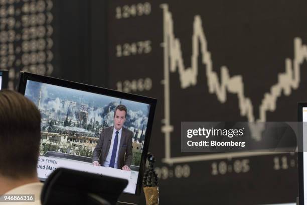 Television news report shows damage from military airstrikes on Syria as the DAX Index curve is displayed beyond at the Frankfurt Stock Exchange,...