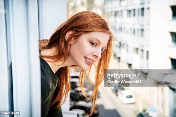 portrait of smiling redheaded woman leaning out of window - woman bending over 個照片及圖片檔