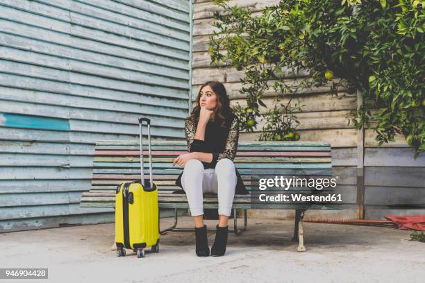 young woman with yellow trolley bag waiting on a bench - young woman trolley stock-fotos und bilder