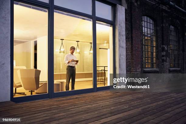 exterior view of man using tablet in modern building at night - looking outside window stock-fotos und bilder