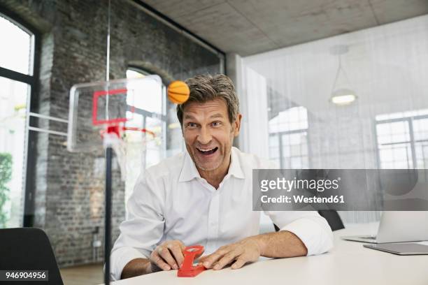 happy businessman playing mini basketball game in modern office - ball on a table stockfoto's en -beelden
