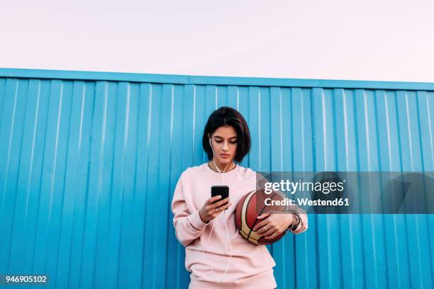 young woman with basketball, smartphone and earphones at container - sport fashion stockfoto's en -beelden