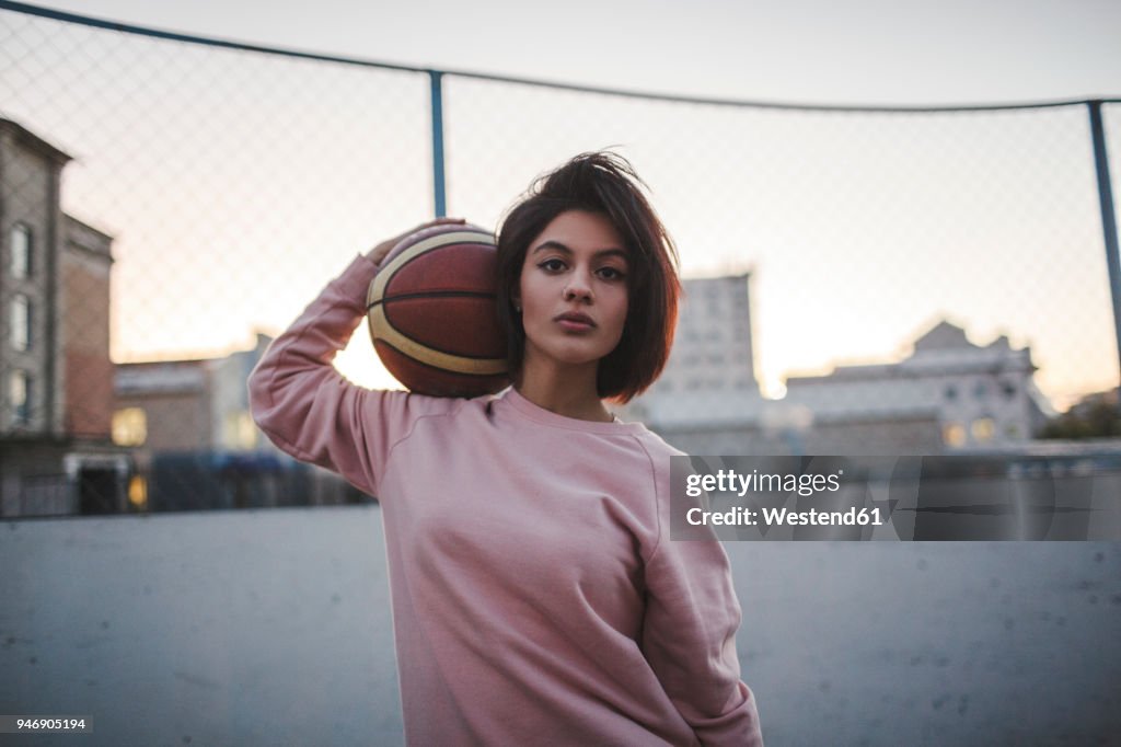 Portrait of young woman holding basketball outdoors