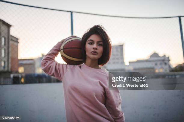 portrait of young woman holding basketball outdoors - basketball sport stock-fotos und bilder
