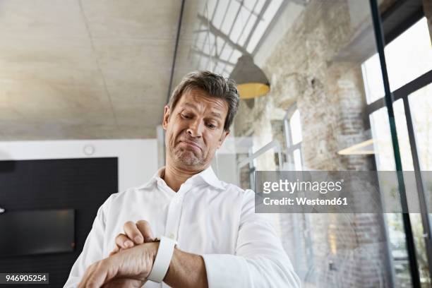 sceptical businessman in office using smartwatch - wrist watch stock-fotos und bilder