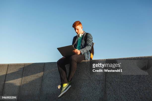 redheaded young man sitting on wall using laptop - フリーランス ストックフォトと画像