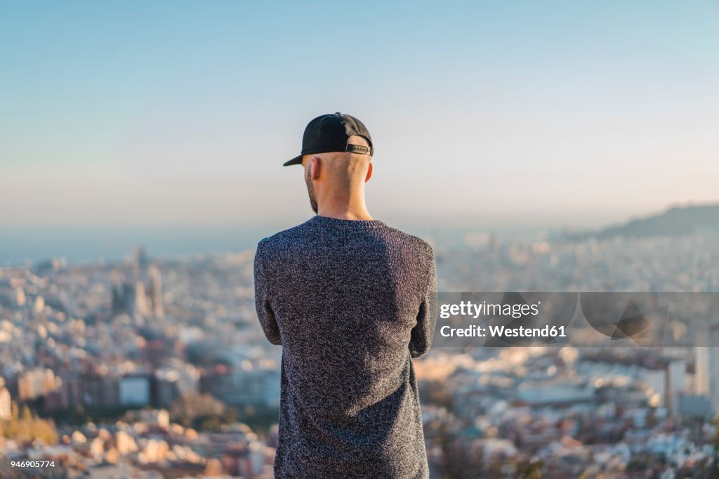 Spain, Barcelona, young man standing on a hill overlooking the city