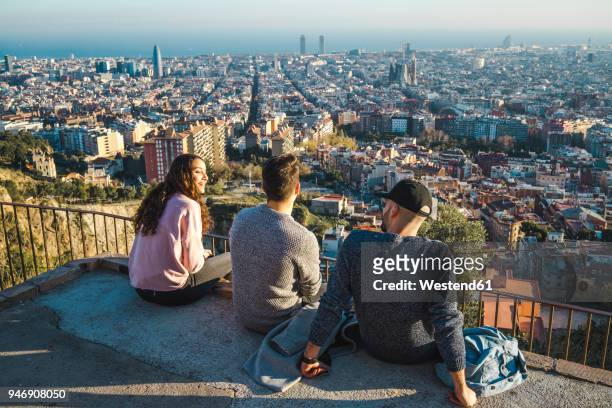 spain, barcelona, three friends sitting on a wall overlooking the city - barcelona spain fotografías e imágenes de stock