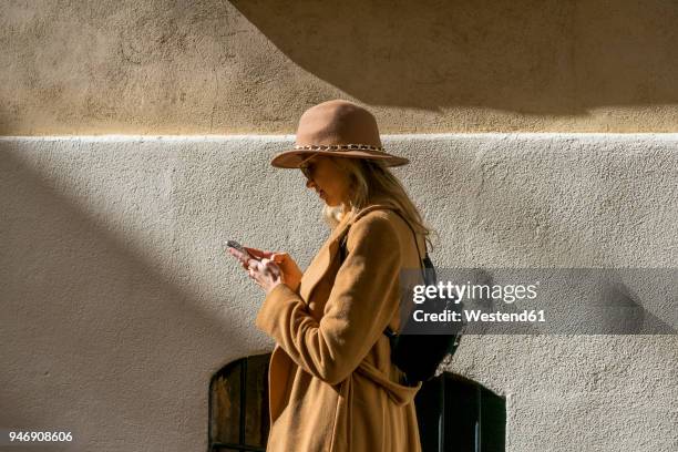 fashionable young woman at a building using cell phone - bruine hoed stockfoto's en -beelden