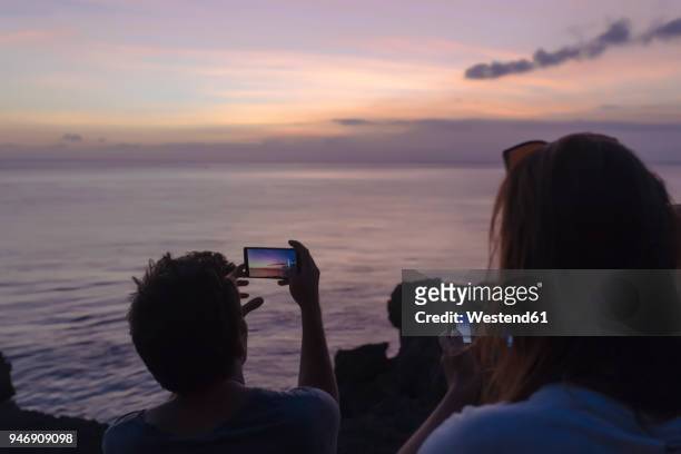 indonesia, bali, lembongan island, friends at ocean coast at dusk taking cell phone pictures - romantic sky stock pictures, royalty-free photos & images