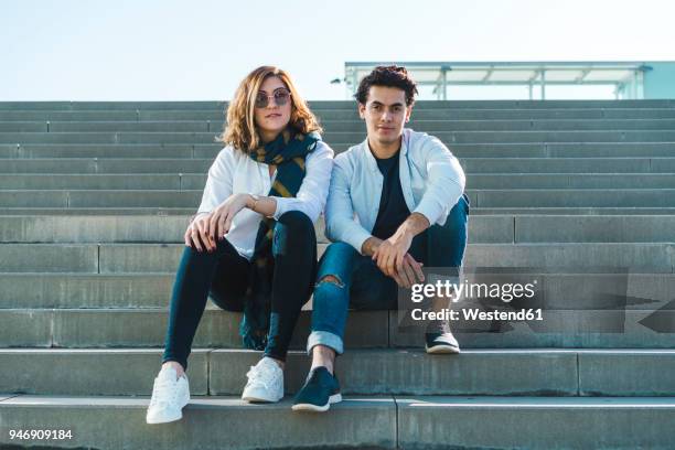 portrait of stylish young couple sitting on stairs outdoors - barcelona fashion day 2 stockfoto's en -beelden