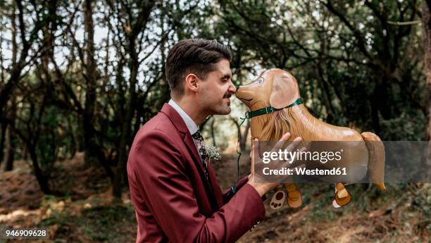 man wearing suit in forest playing with funny dog-shaped balloon - fake man stock pictures, royalty-free photos & images