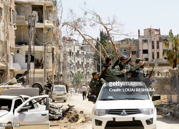 Syrian police flash the sign for victory in the back of a vehicle as they drive down a destroyed street in Douma on the outskirts of Damascus on...