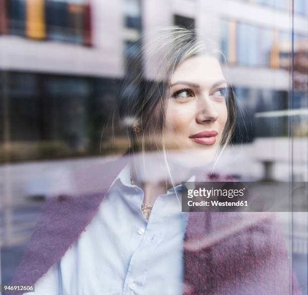 smiling young woman looking out of window - reflection photos et images de collection