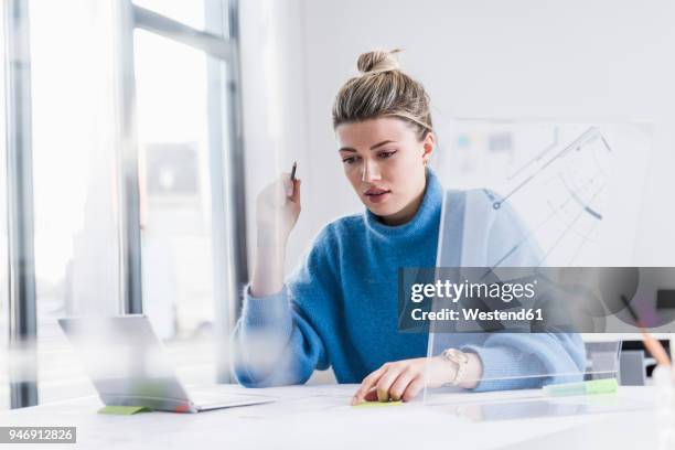 young woman with laptop and transparent design working on plan at desk in office - architects design drawings stock-fotos und bilder