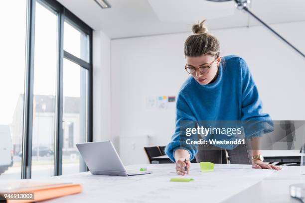 young woman with laptop working on plan at desk in office - vornüber beugen stock-fotos und bilder