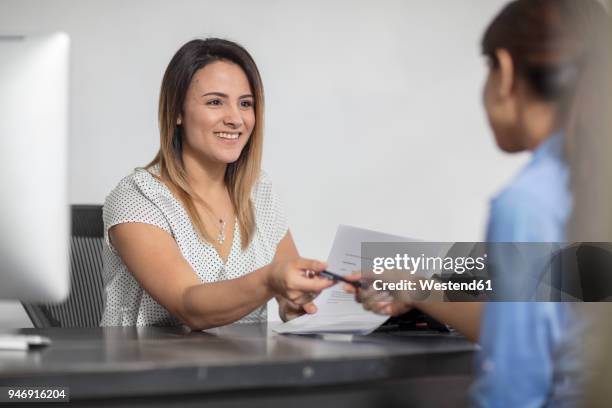 smiling woman handing over pen to client at desk - grant writer stock pictures, royalty-free photos & images