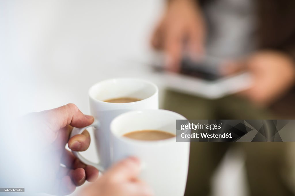 Close-up of woman holding coffee cups while man using tablet in office