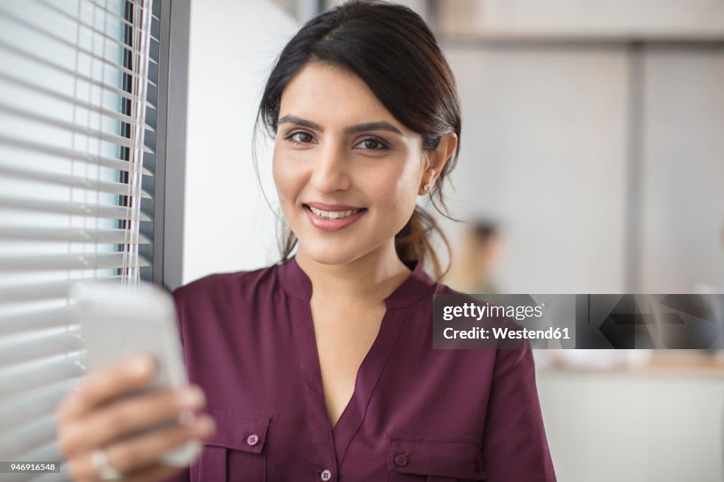 Portrait of smiling businesswoman holding cell phone in office