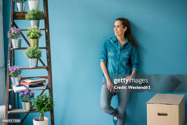 beautiful woman in her new home, decorated with plants, leaning at wall - repairing clothes stock pictures, royalty-free photos & images