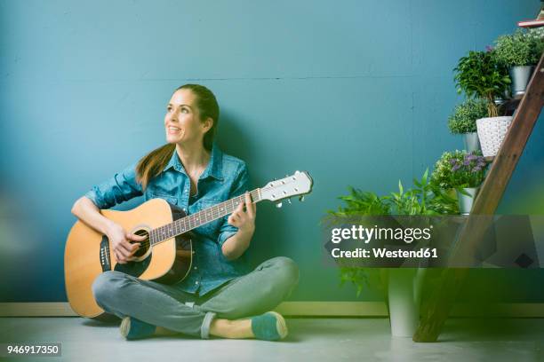 woman relaxing in her home with potted plants, playing guitar - spring hygge stock pictures, royalty-free photos & images