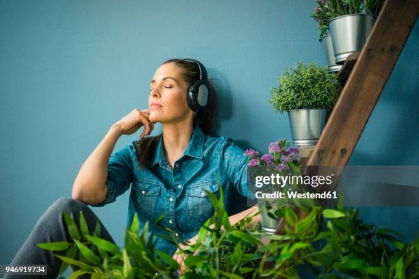 beautiful woman in her home, decorated with plants, listening music with headphones - frau kopfhörer indoor stock-fotos und bilder