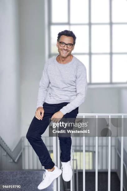 portrait of smiling man sitting on railing of staircase - stubble stockfoto's en -beelden