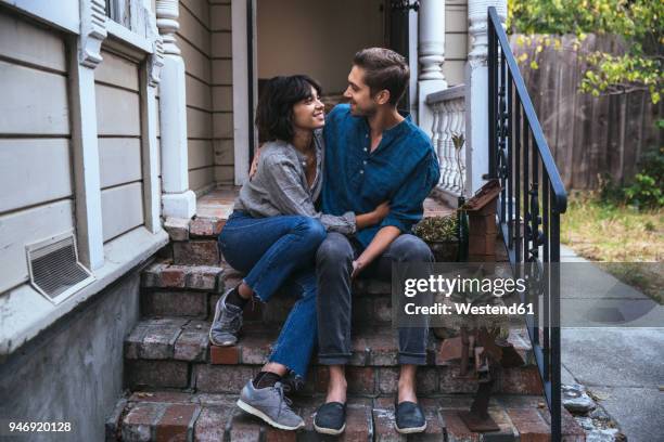 happy couple sitting on stoop embracing - millennial generation couple stock pictures, royalty-free photos & images